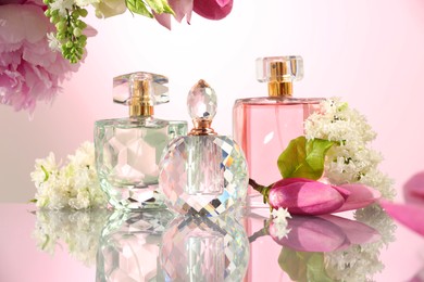 Photo of Luxury perfumes and floral decor on mirror surface against pink background