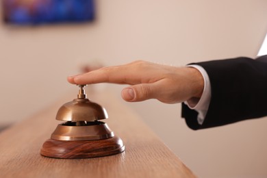 Photo of Man ringing service bell at wooden reception desk in hotel, closeup