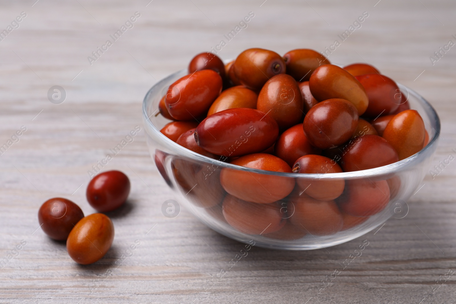 Photo of Fresh Ziziphus jujuba fruits with glass bowl on wooden table, closeup