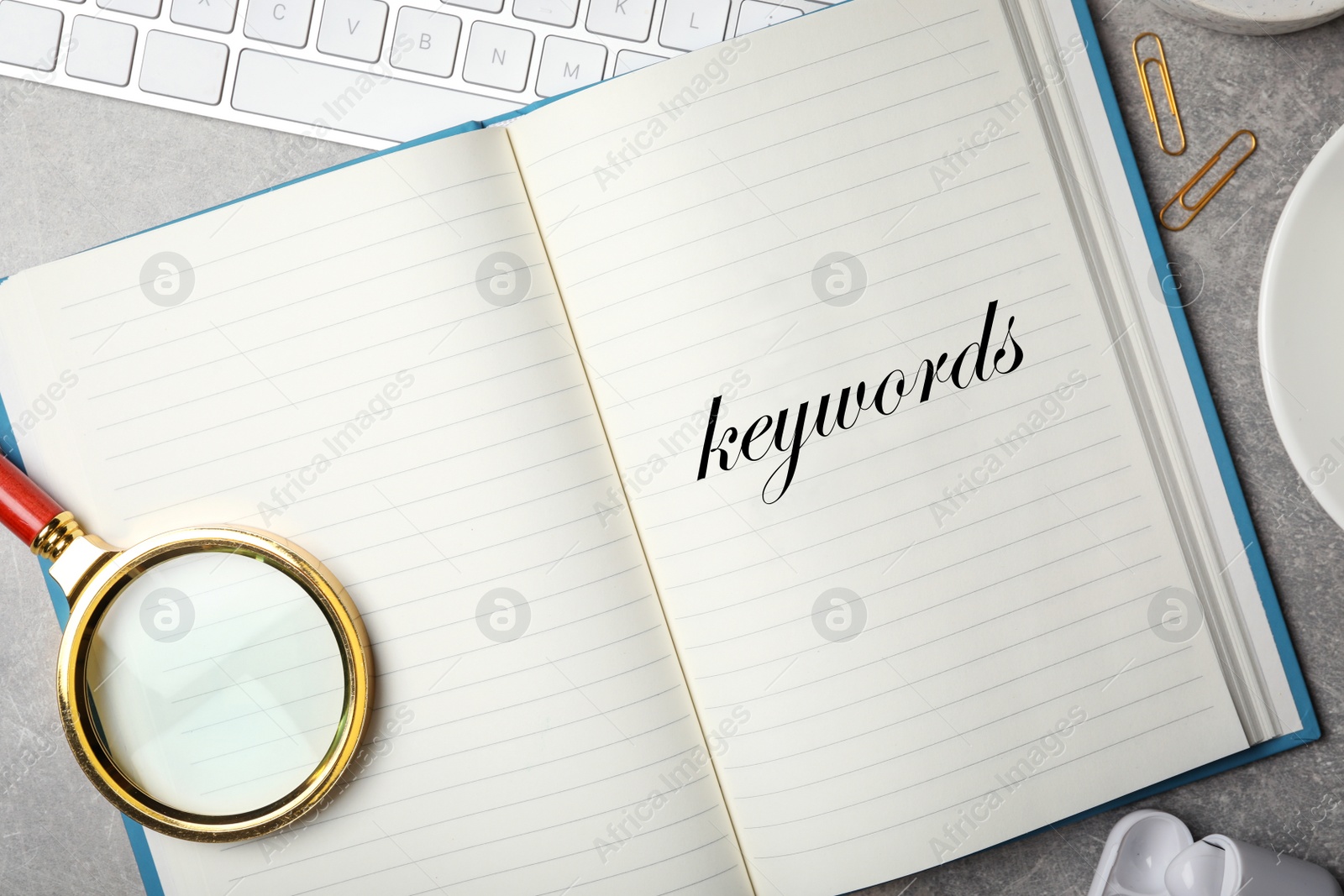 Image of Notebook with text KEYWORDS and magnifying glass on grey stone table, flat lay