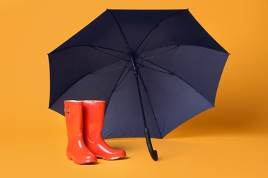 Photo of Open blue umbrella and red rubber boots on yellow background