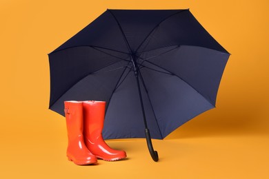 Open blue umbrella and red rubber boots on yellow background