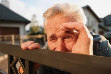 Concept of private life. Curious senior man spying on neighbours over fence outdoors, closeup