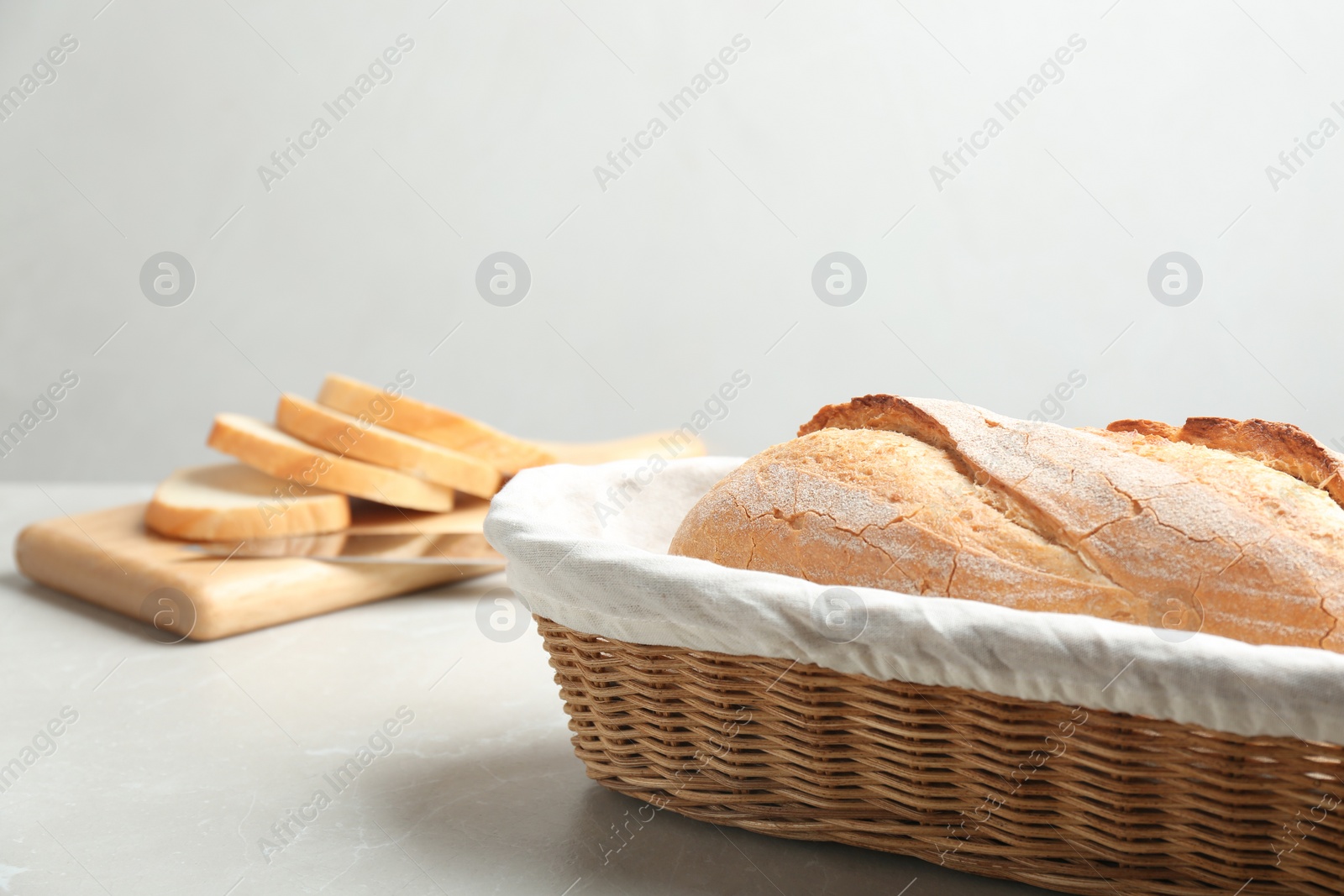 Photo of Loaf of tasty fresh bread in wicker basket on light marble table. Space for text