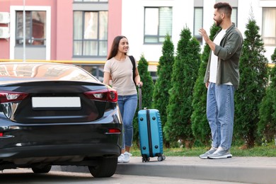 Photo of Long-distance relationship. Man waving to his girlfriend with luggage near car outdoors