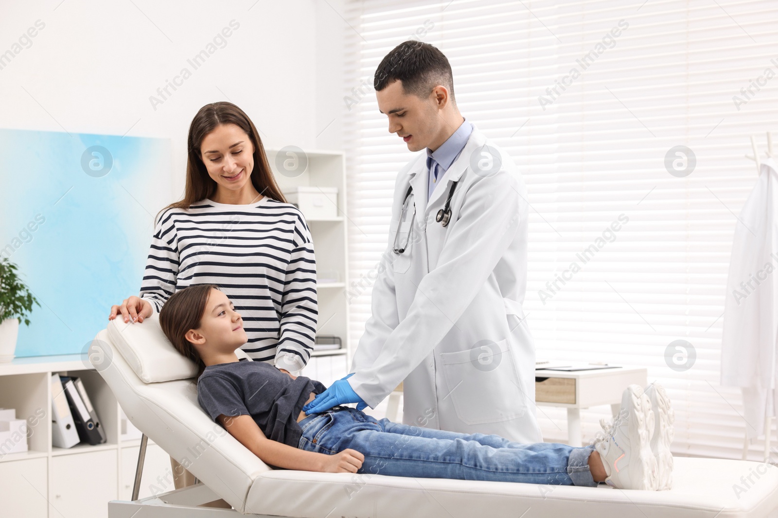 Photo of Gastroenterologist examining girl with stomach ache on couch in clinic