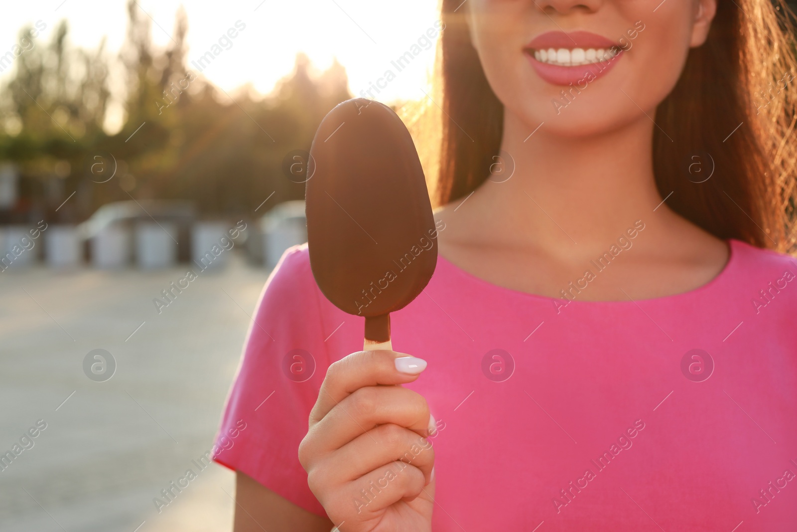 Photo of Young woman holding ice cream glazed in chocolate on city street, closeup