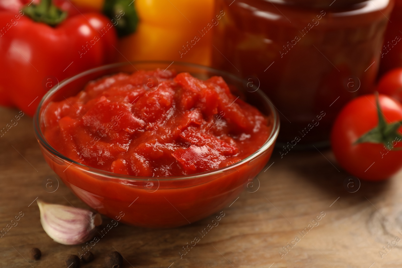 Photo of Delicious lecho in glass bowl and fresh ingredients on wooden table, closeup