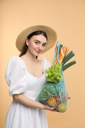 Woman with string bag of fresh vegetables and baguette on beige background