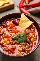 Photo of Bowl of tasty chili con carne with nachos on wooden table, closeup