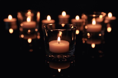 Photo of Burning candles in glass holders on dark background