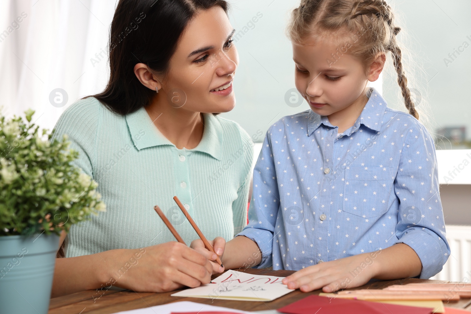 Photo of Cute little girl with her mother making beautiful greeting card at home