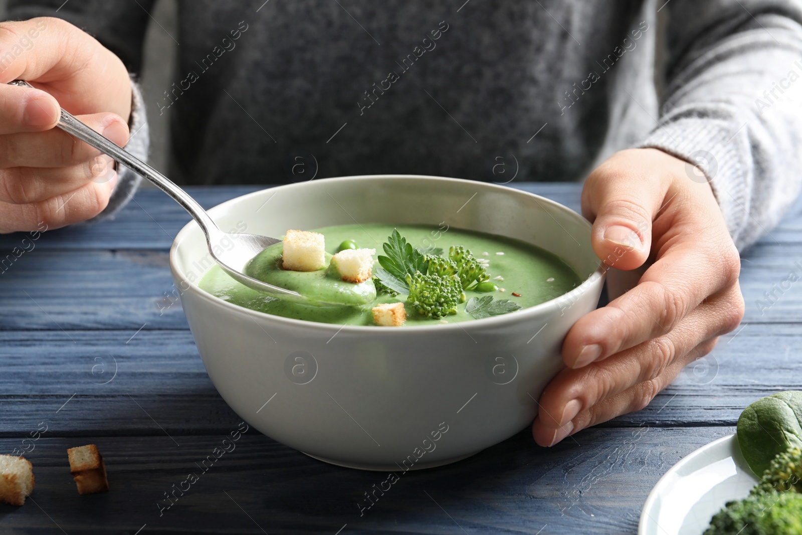 Photo of Woman eating fresh vegetable detox soup made of broccoli with croutons at table, closeup