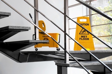 Photo of Safety sign with phrase Caution wet floor and mop bucket on stairs. Cleaning service