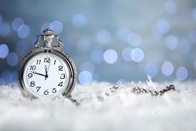 Photo of Pocket watch on snow against blurred lights, space for text. New Year countdown