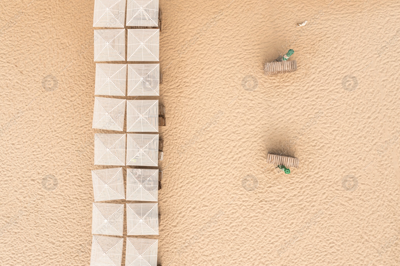 Image of Many beach umbrellas and wooden sunbeds on sandy coast, aerial view