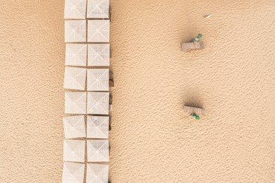 Image of Many beach umbrellas and wooden sunbeds on sandy coast, aerial view