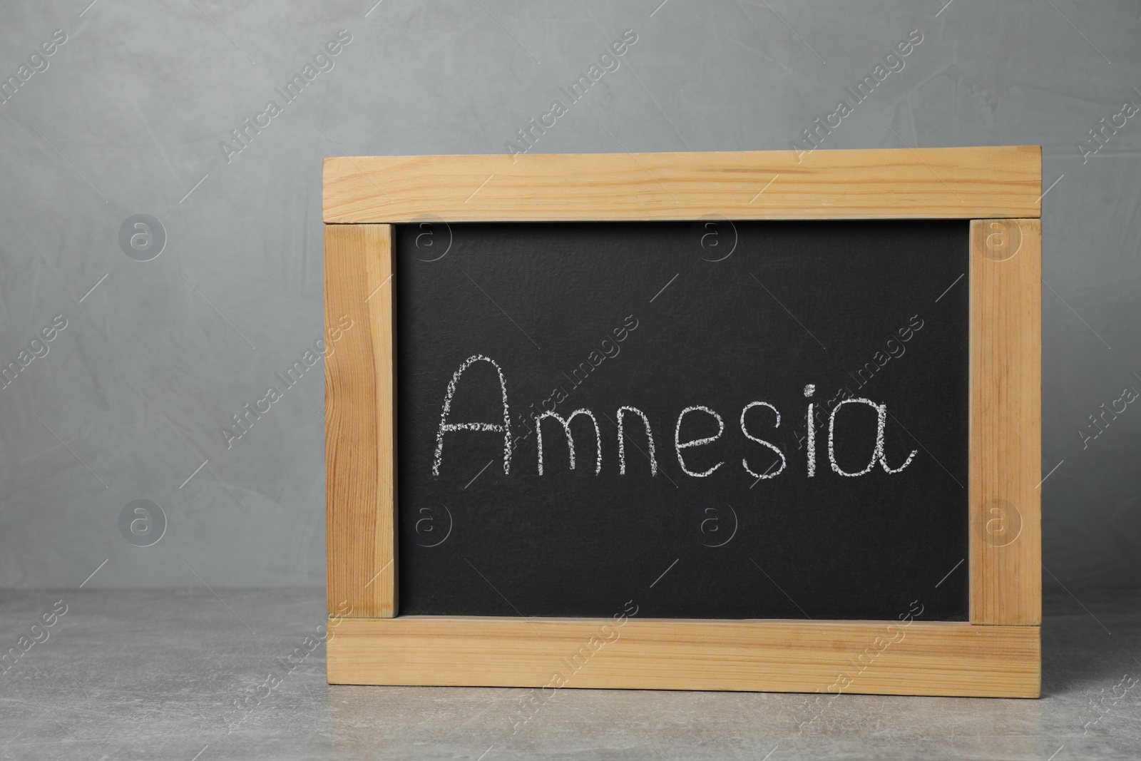 Photo of Small blackboard with word Amnesia on grey table