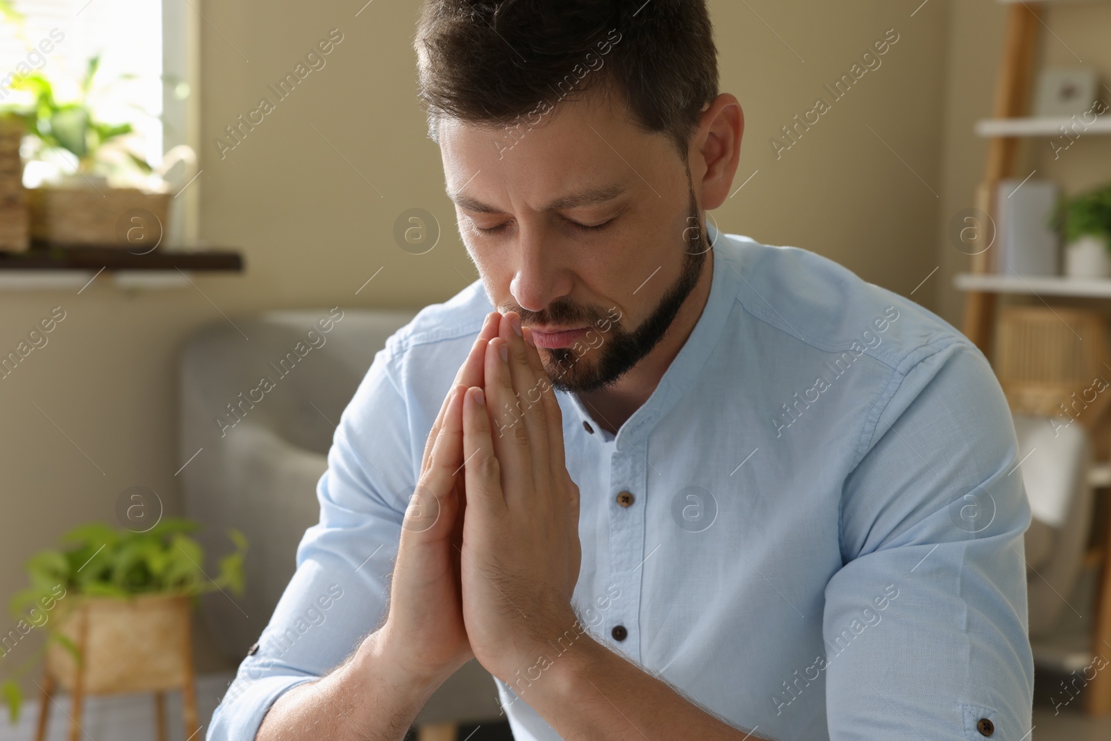 Photo of Religious man with clasped hands praying indoors