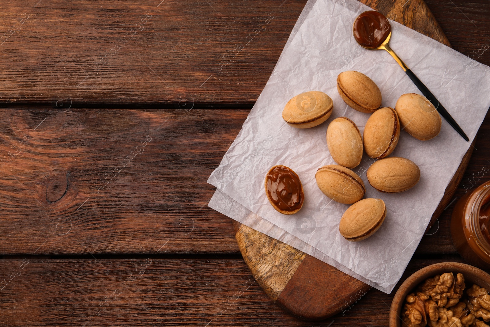 Photo of Delicious nut shaped cookies with boiled condensed milk on wooden table, flat lay. Space for text