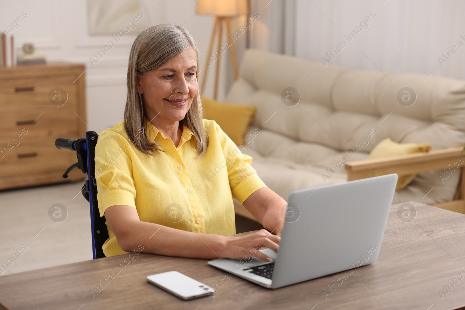 Photo of Woman in wheelchair using laptop at table in home office