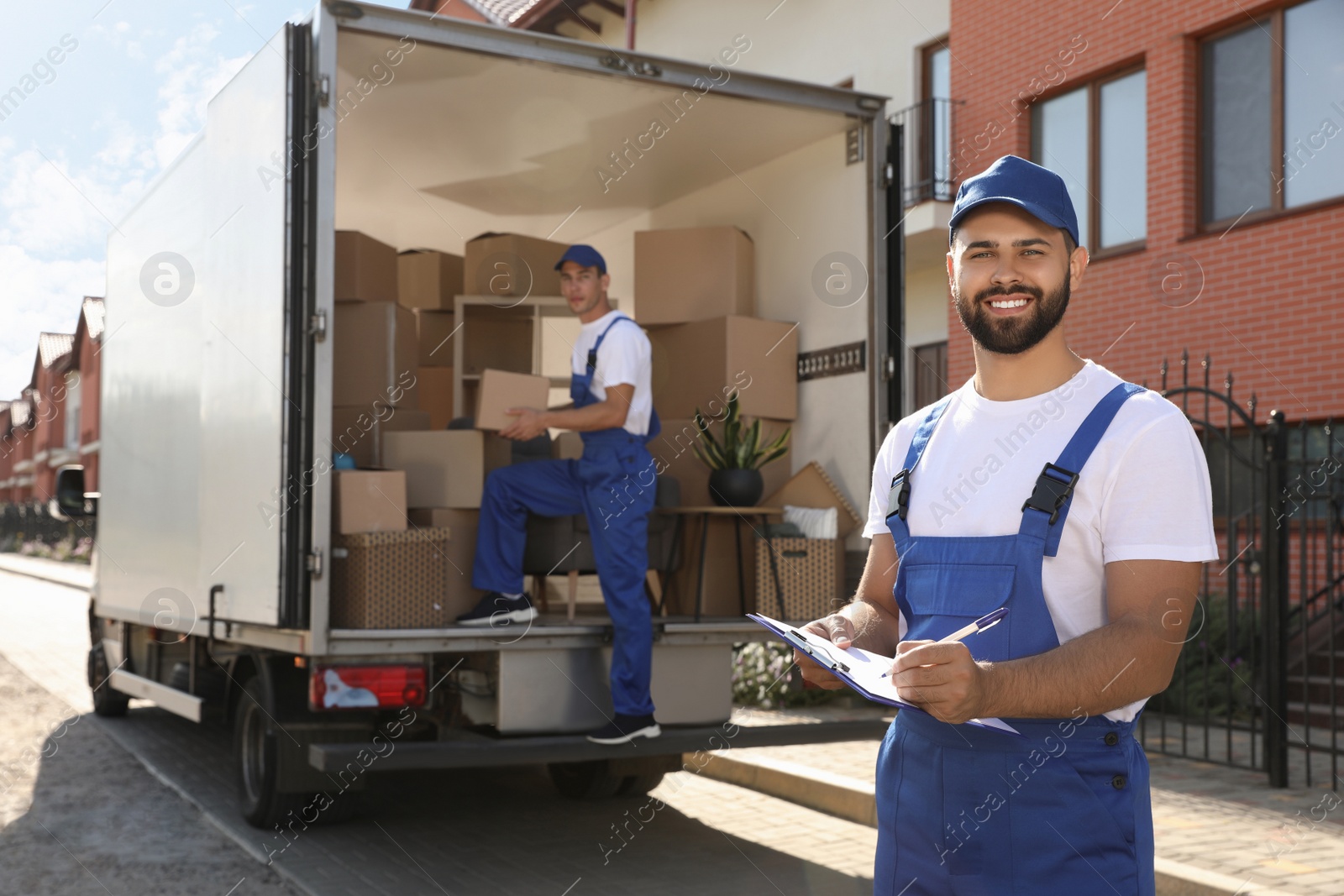 Photo of Moving service workers outdoors, unloading boxes and checking list