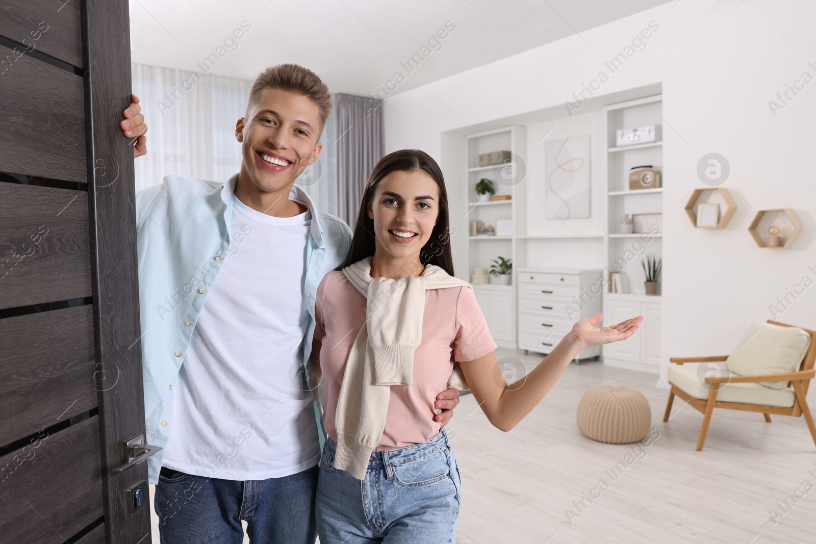 Photo of Happy couple welcoming near door. Invitation to come indoors