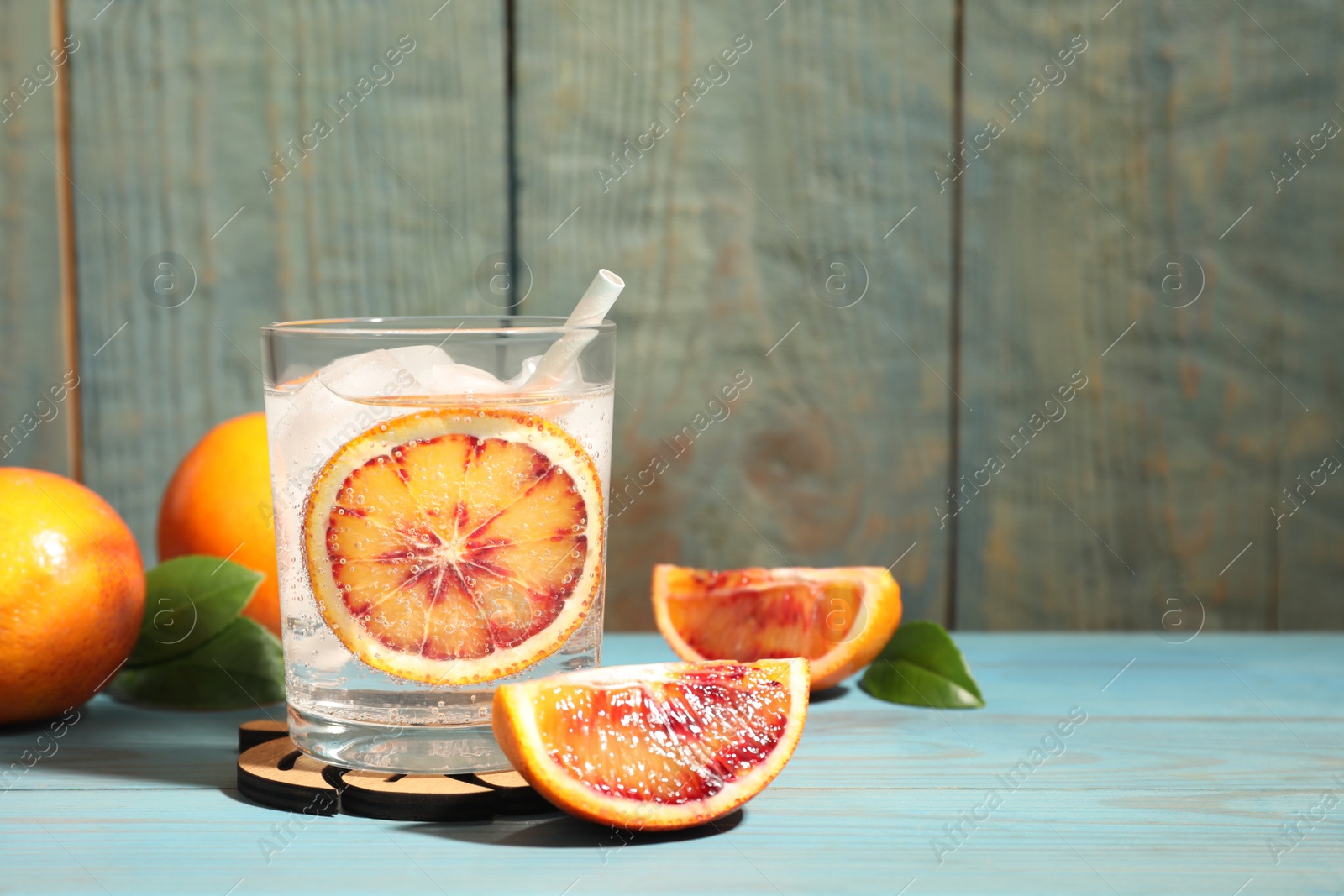 Photo of Delicious refreshing drink with sicilian orange, fresh fruits and green leaves on light blue wooden table. Space for text