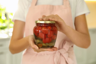 Woman holding jar of pickled tomatoes indoors, closeup