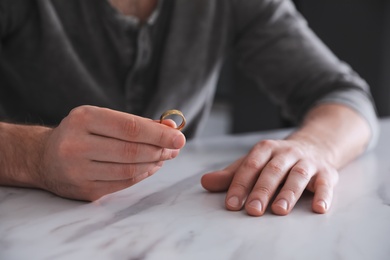 Photo of Man holding wedding ring at white marble table, closeup. Divorce concept