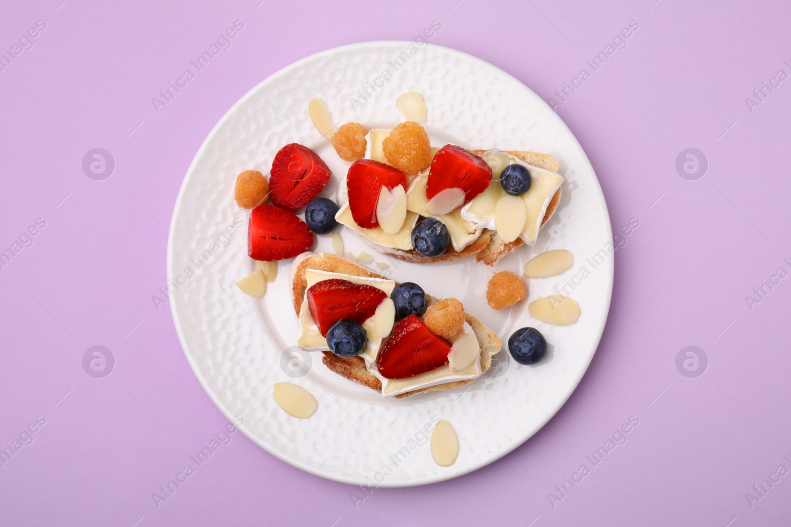 Photo of Tasty sandwiches with brie cheese, fresh berries and almond flakes on violet background, top view