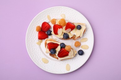 Tasty sandwiches with brie cheese, fresh berries and almond flakes on violet background, top view