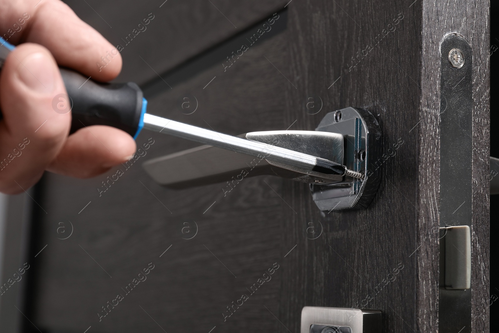 Photo of Handyman with screwdriver repairing door handle indoors, closeup