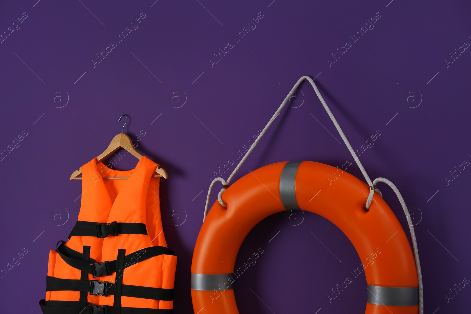 Photo of Orange life jacket and lifebuoy on violet background. Rescue equipment