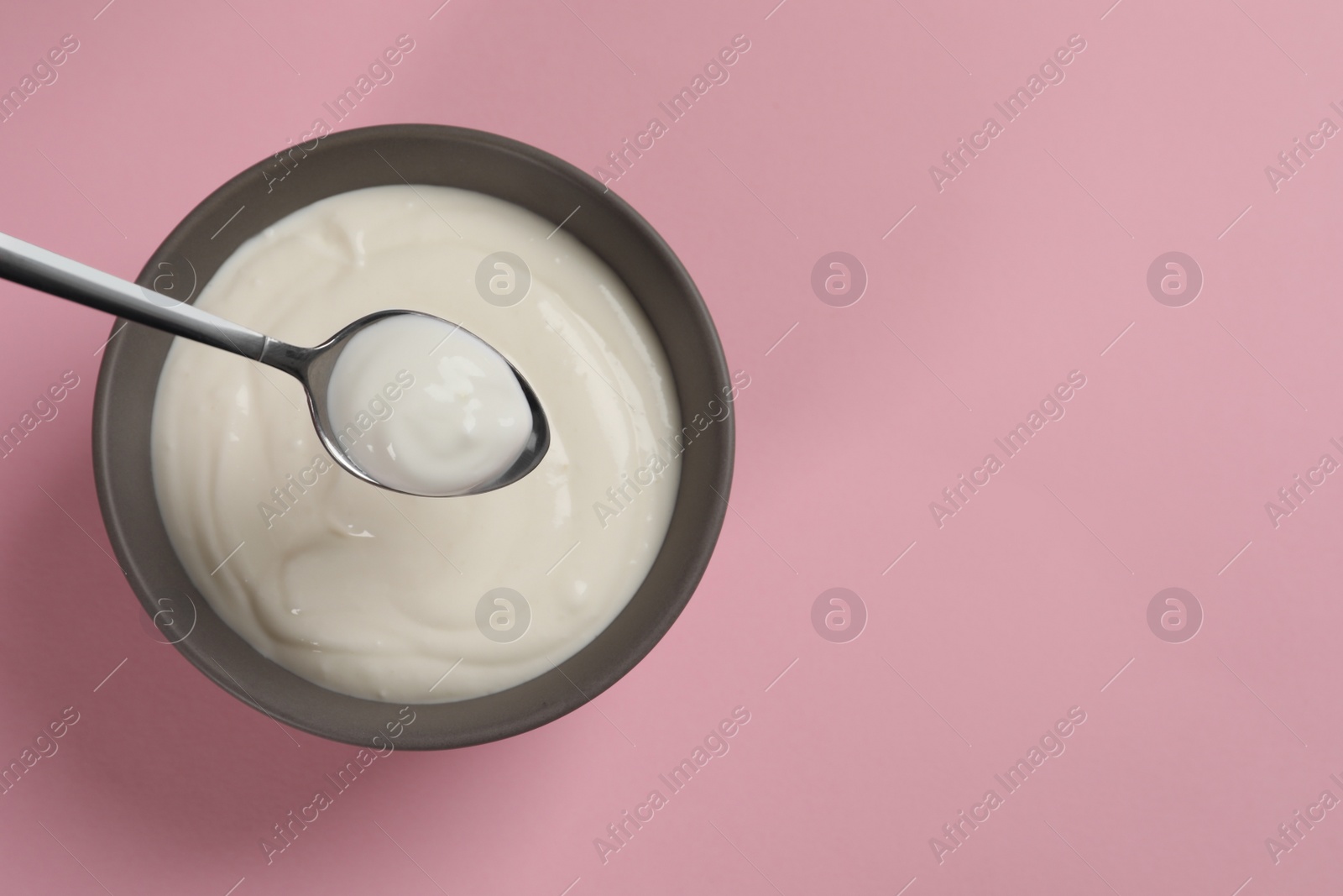 Photo of Eating tasty yogurt from bowl on pink background, top view. Space for text