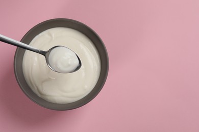 Photo of Eating tasty yogurt from bowl on pink background, top view. Space for text