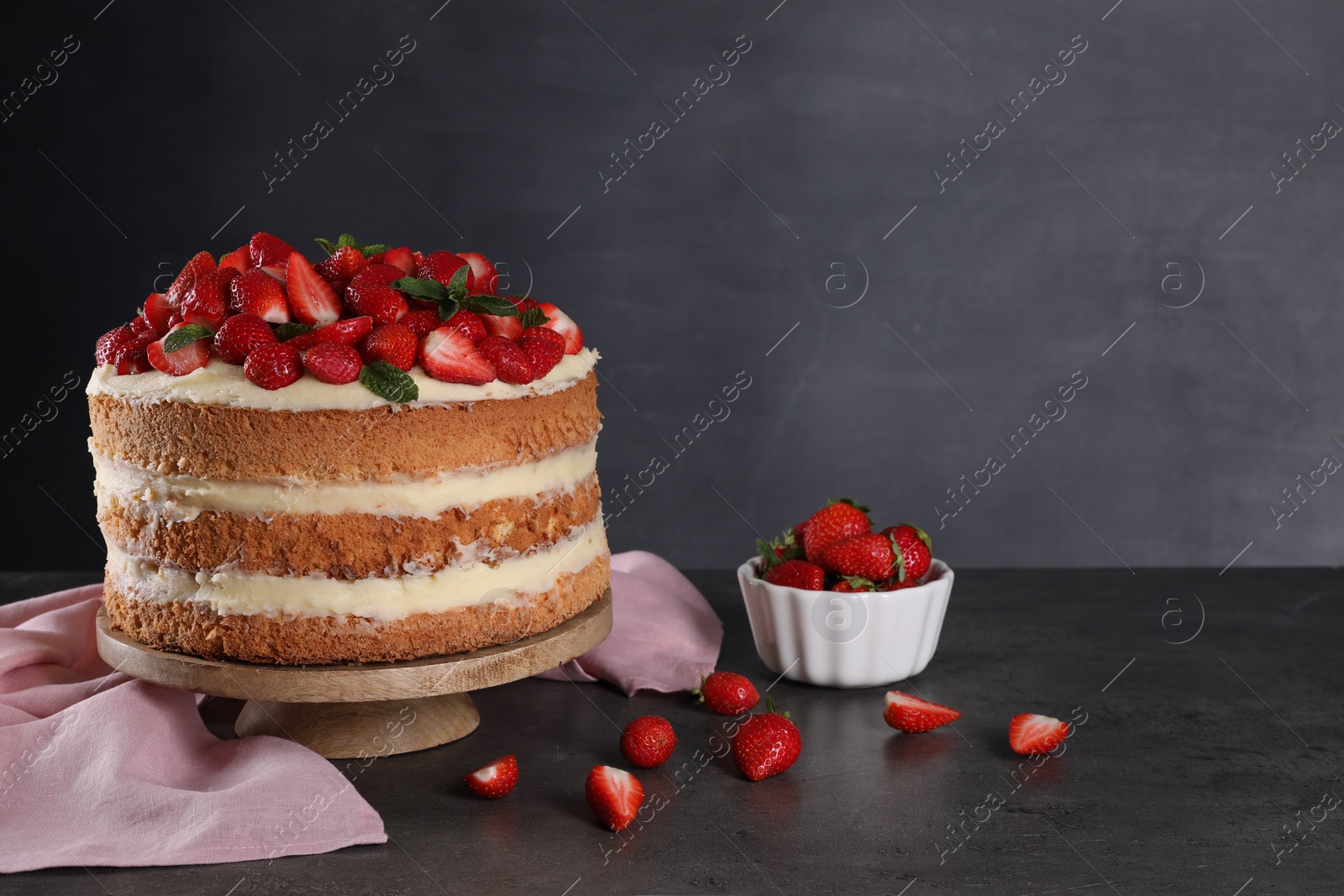 Photo of Tasty cake with fresh strawberries and mint on table against dark gray background