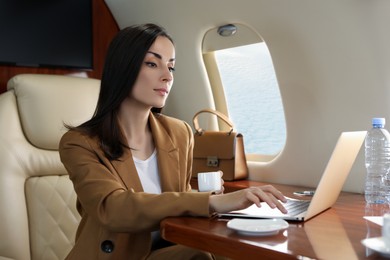 Businesswoman with cup of coffee working on laptop at table in airplane during flight