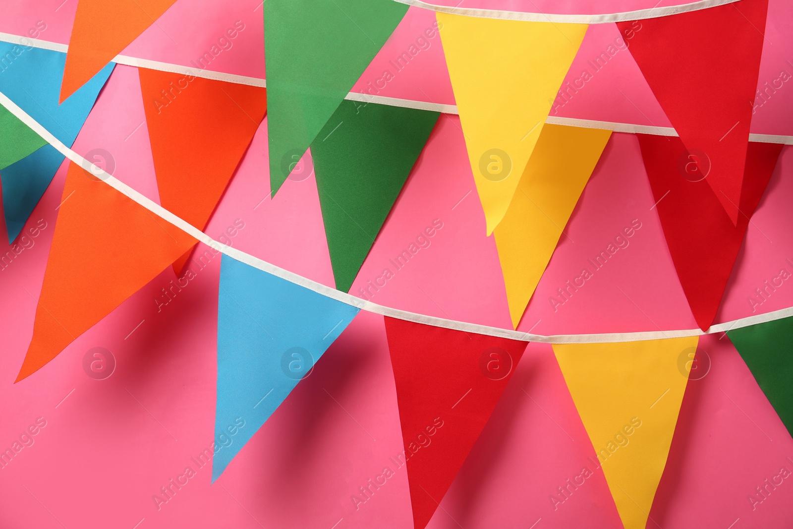 Photo of Buntings with colorful triangular flags hanging on pink background. Festive decor