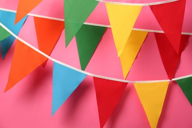 Photo of Buntings with colorful triangular flags hanging on pink background. Festive decor