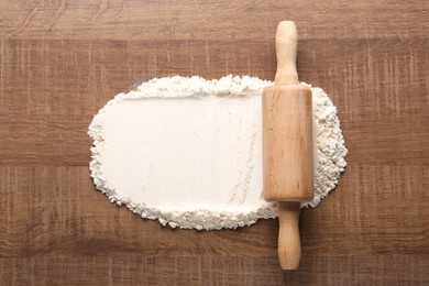 Photo of Flour and rolling pin on wooden table, top view