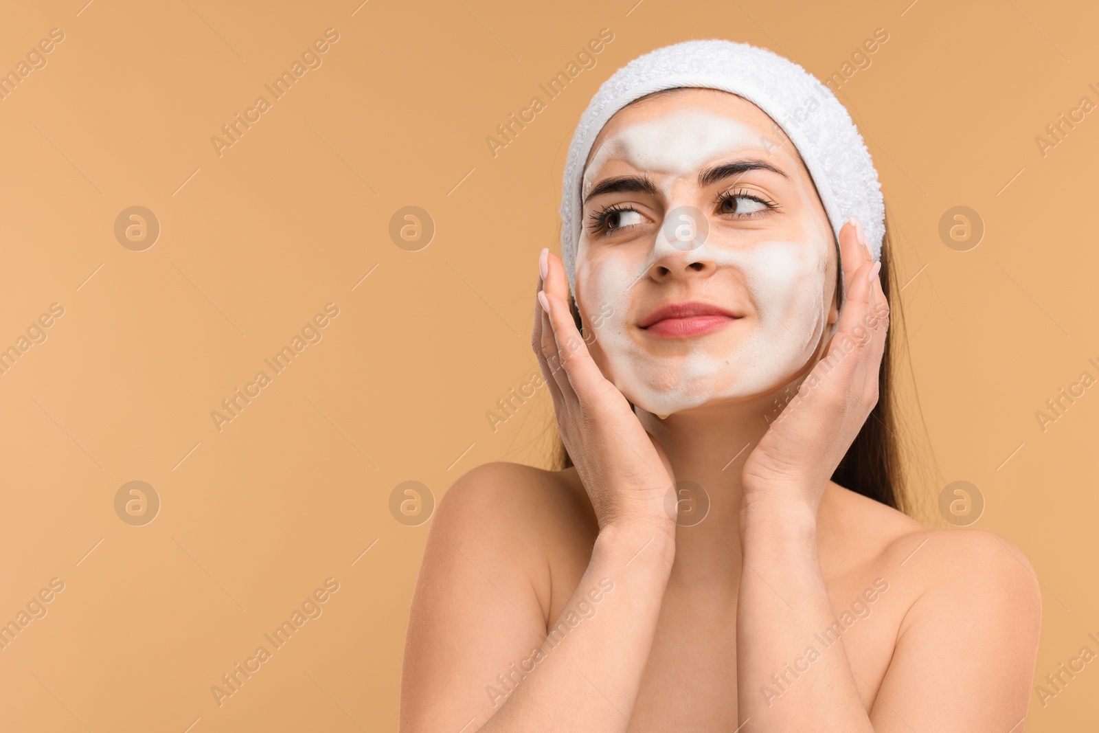 Photo of Young woman with headband washing her face on beige background, space for text