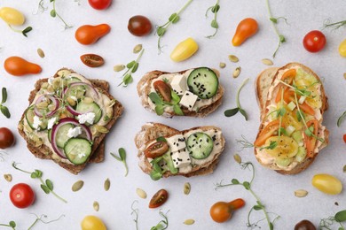 Tasty vegan sandwiches with vegetables and microgreens on light grey table, flat lay