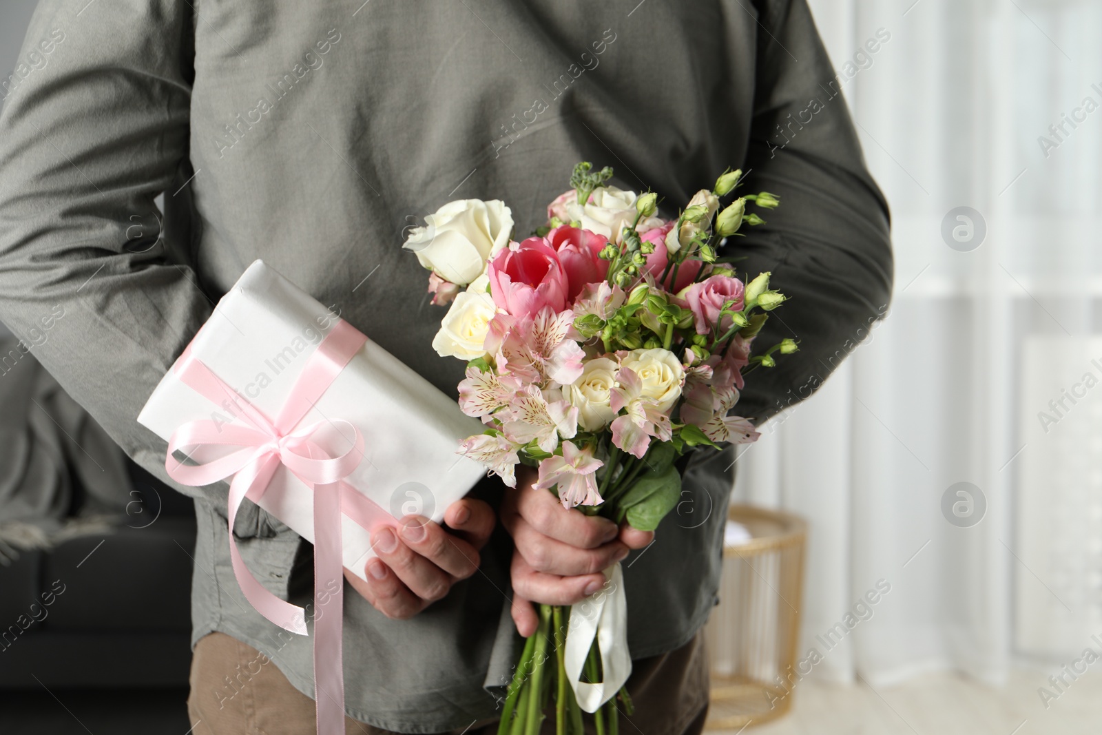 Photo of Man hiding bouquet of flowers and present indoors, closeup