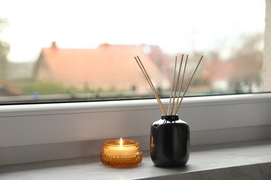 Photo of Aromatic reed air freshener and scented candle on windowsill indoors