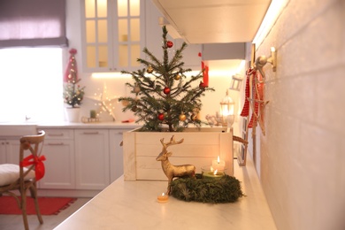 Small Christmas tree decorated with baubles and festive lights in kitchen