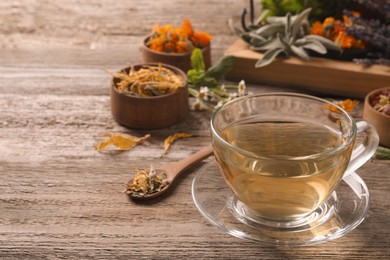 Photo of Glass cup of aromatic freshly brewed tea near different dry herbs on wooden table. Space for text
