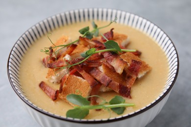 Photo of Delicious lentil soup with bacon and microgreens in bowl on gray table, closeup