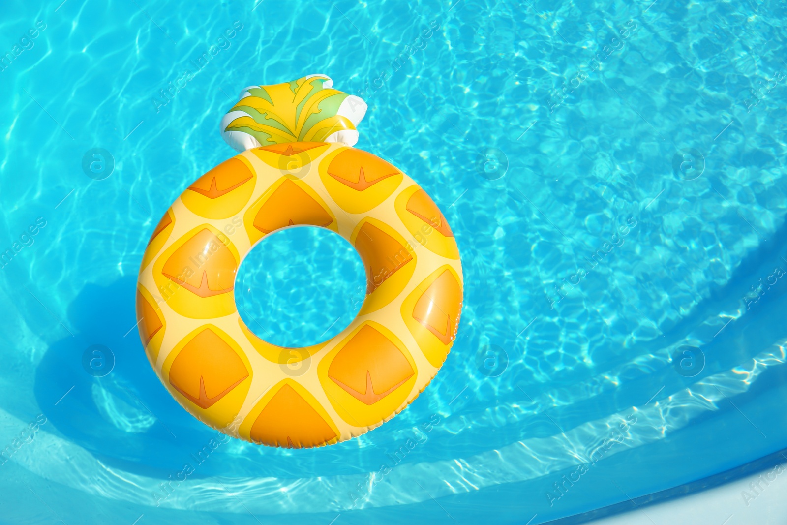 Photo of Bright inflatable pineapple ring floating in swimming pool on sunny day, above view. Space for text