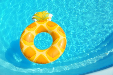 Bright inflatable pineapple ring floating in swimming pool on sunny day, above view. Space for text